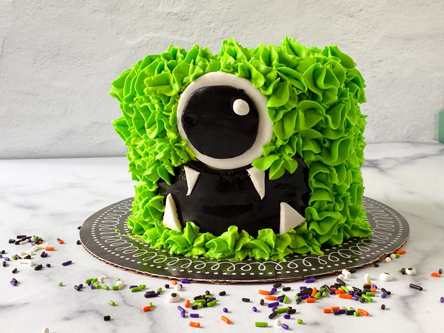 Front view of a cake piped with green frosting and fondant eye and mouth too resemble a monster.