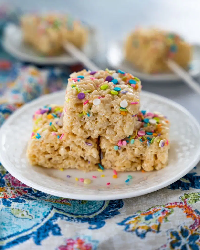 Table view of 3 Rice Krispie Cookies garnished with colorful sprinkles stacked on a plate.