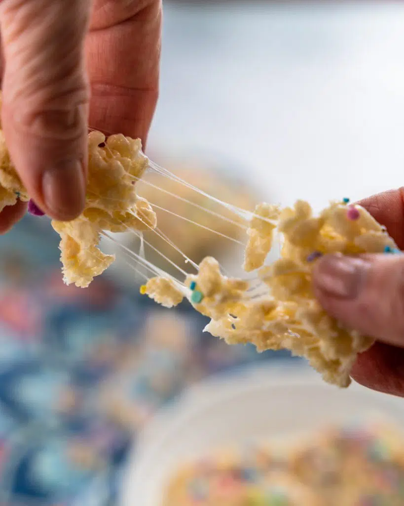 A rice krispie treat being pulled apart showing the stretch of melted marshmallow .