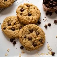 Top down view of three oatmeal chocolate chip cookies on a tray surrounded by chocolate chips and oats. Hostess At Heart