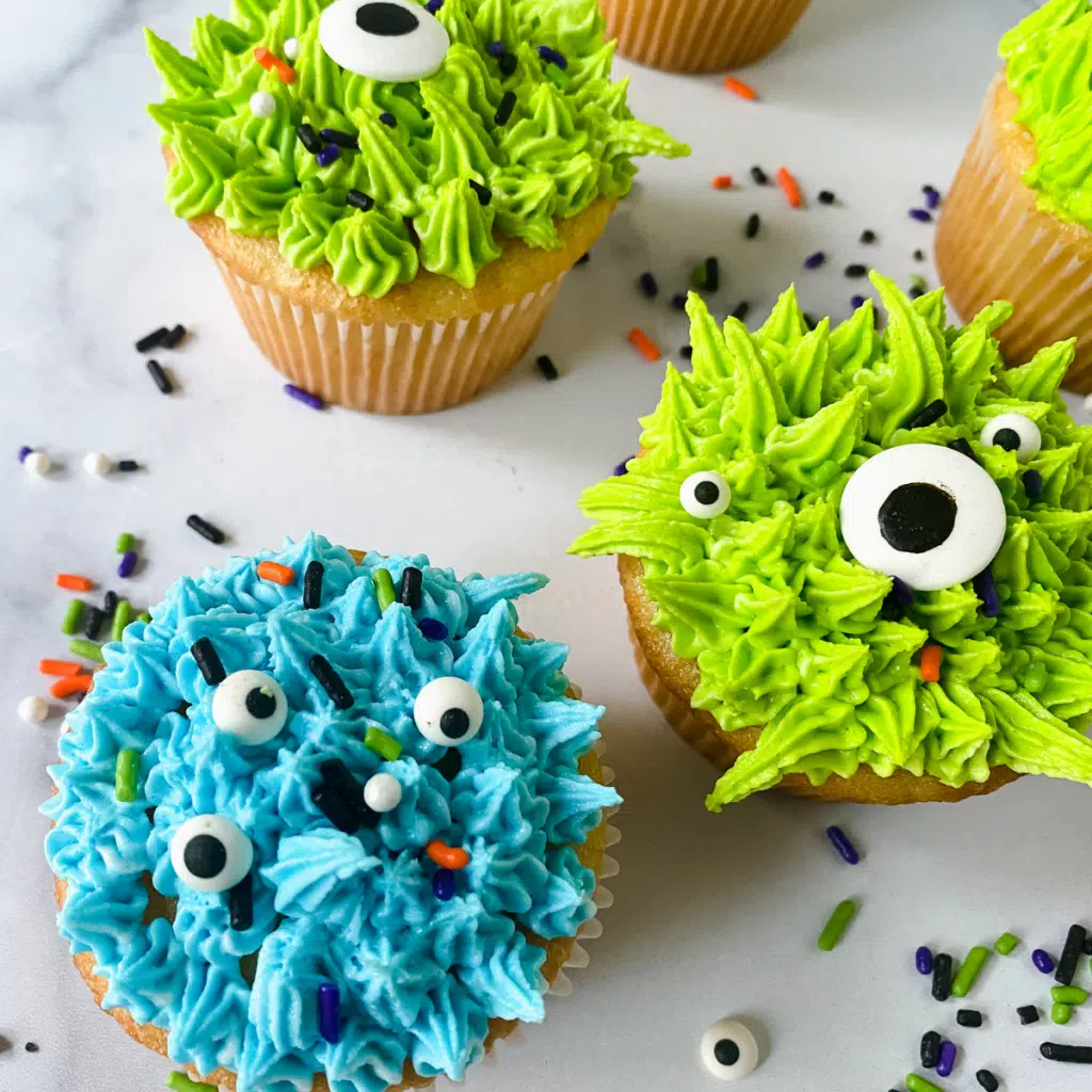 Cupcakes decorated with blue and green frosting and dotted with eyeballs to resemble monsters.