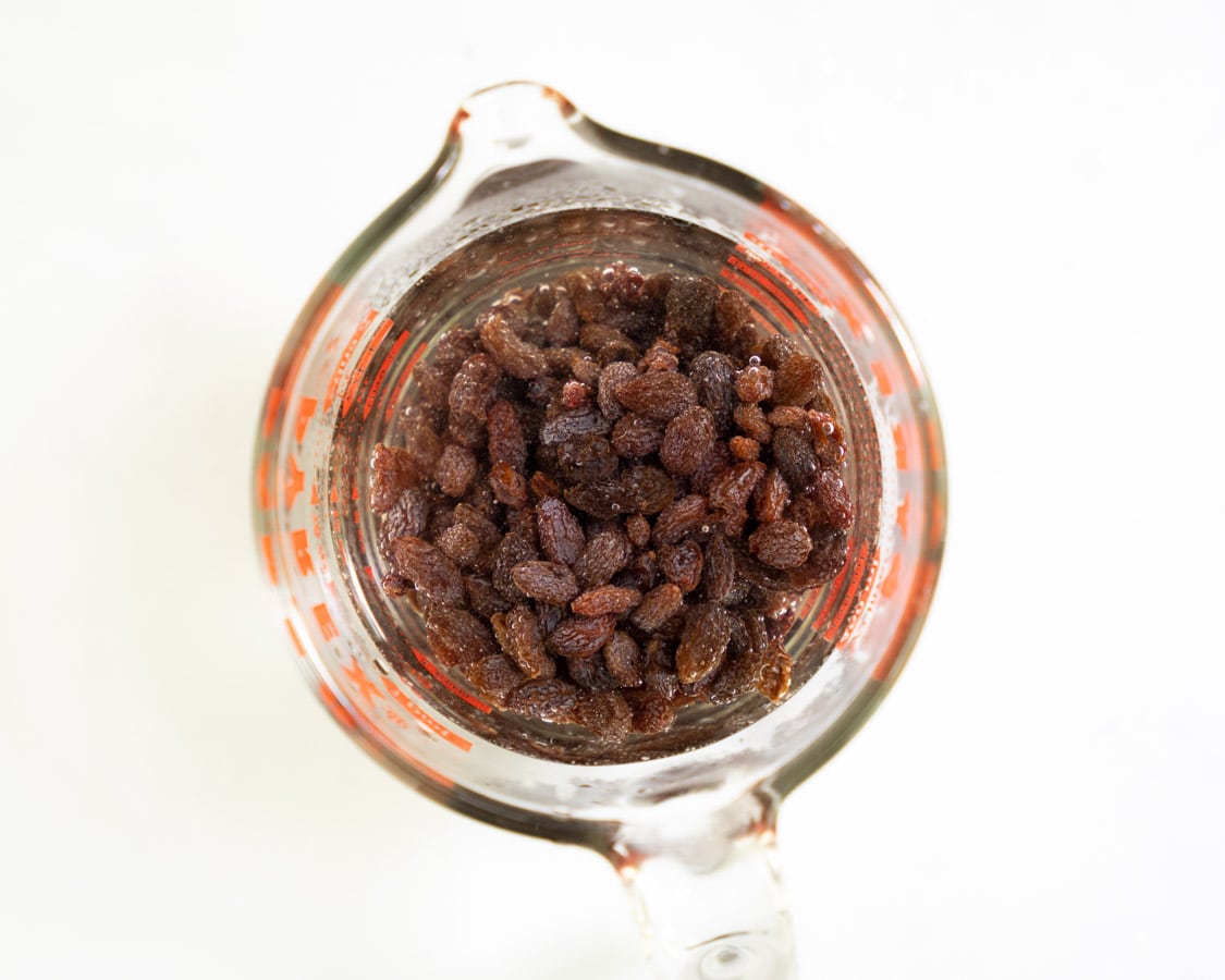 A measuring cup containing raisins covered in hot water.