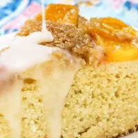 A slice of peach cake with glaze drizzled over the toop.