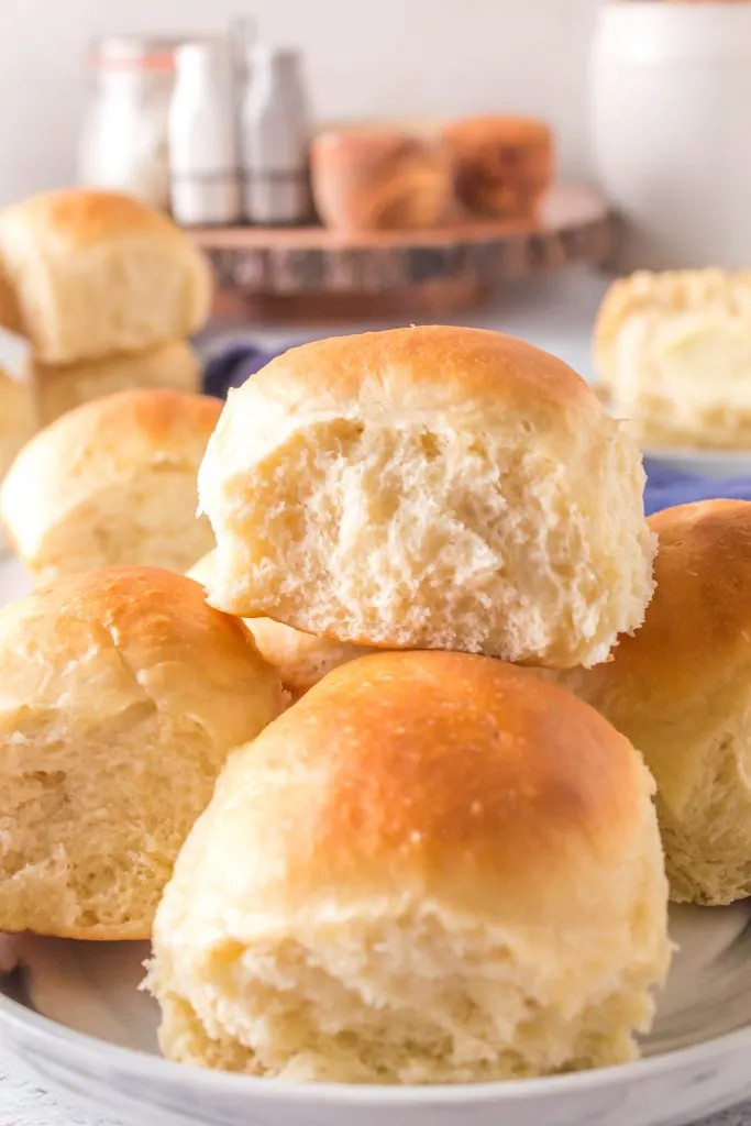 Sideview of a dinner roll sitting on several dinner rolls.