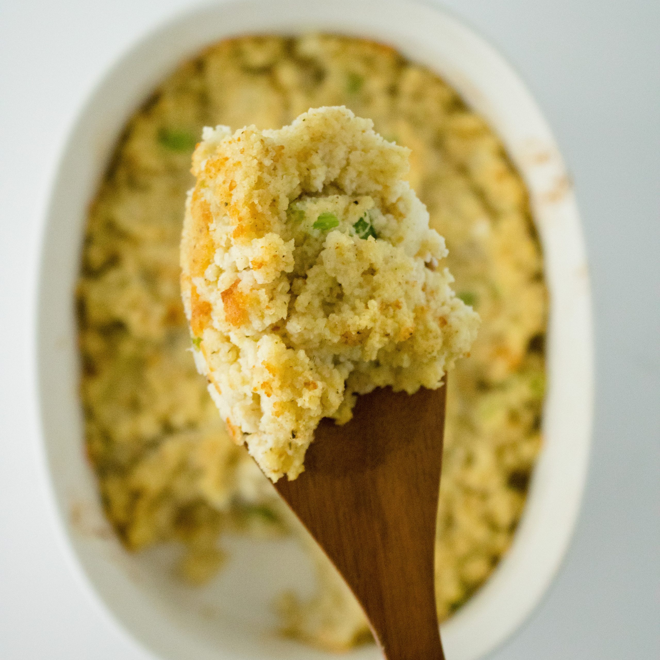 Close-up spoonful of cornbread dressing with a dish of the full cornbread dressing recipe in the background.