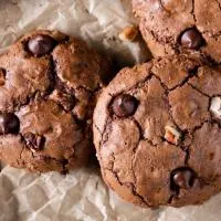 Top down view of three chocolate cookies filled with chocolate chips and nuts.