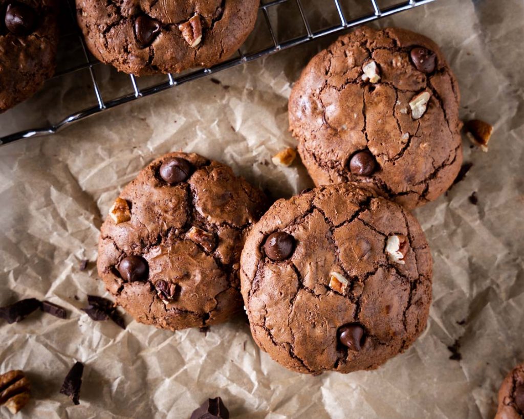 Top down view of three chocolate cookies filled with chocolate chips and nuts.