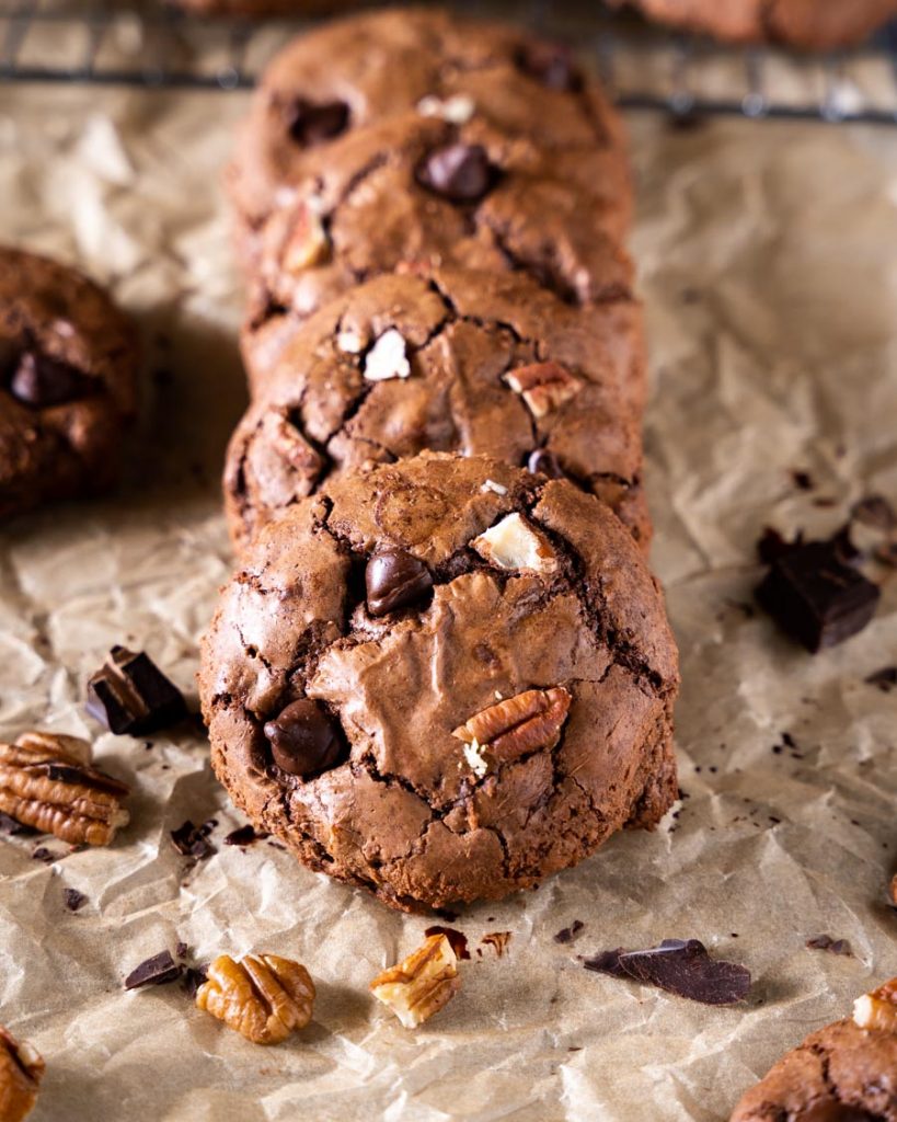 A front view of a row of brownie cookies dotted with chocolate chips and chopped nuts.