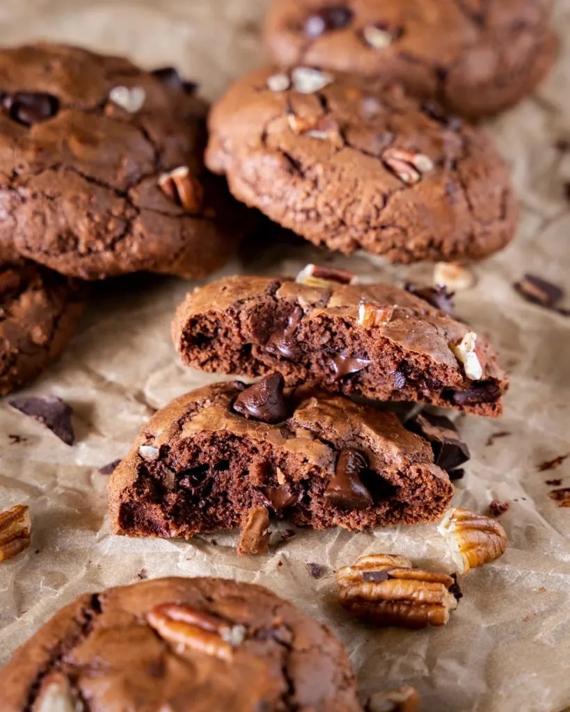 Front view of a chocolate brownie cookie cut in half showing chocolate chips and chopped nuts.