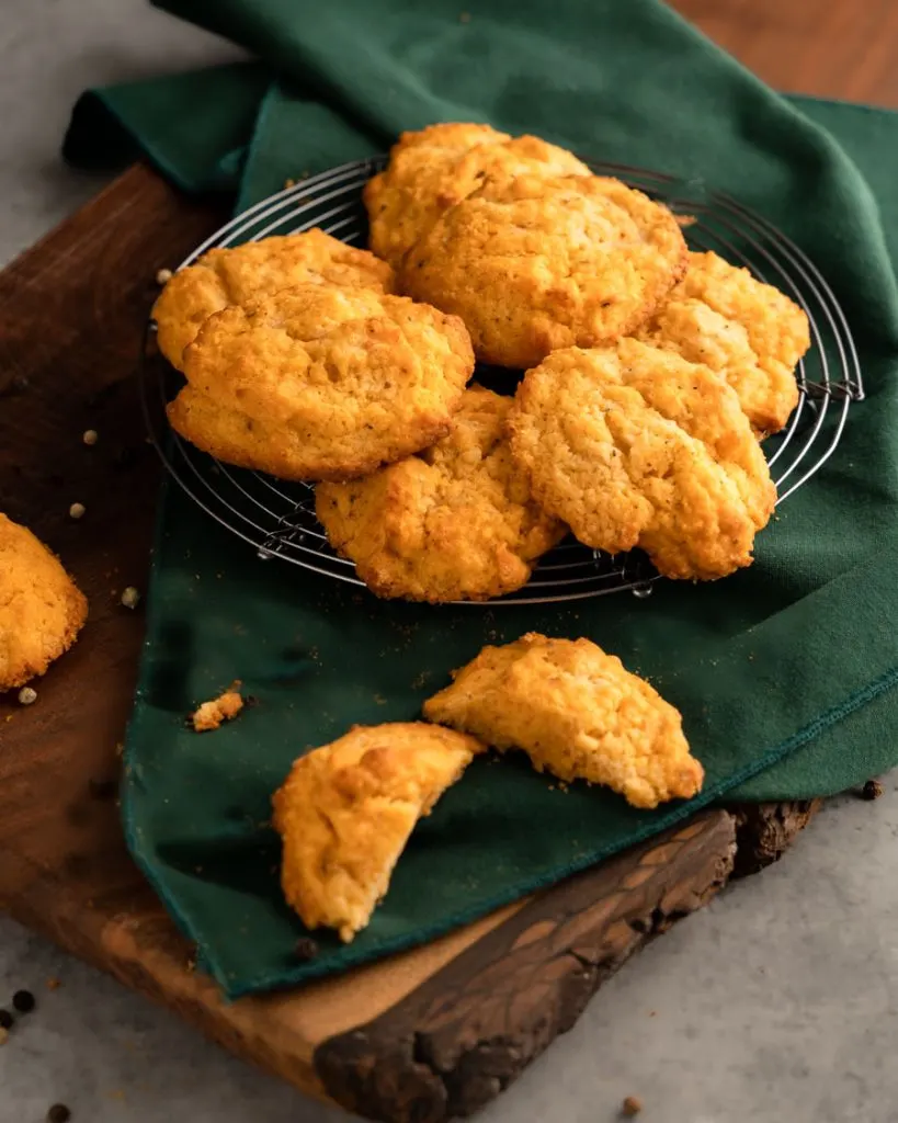 Several biscuits sitting on a cooling rack with a cut biscuit in front.