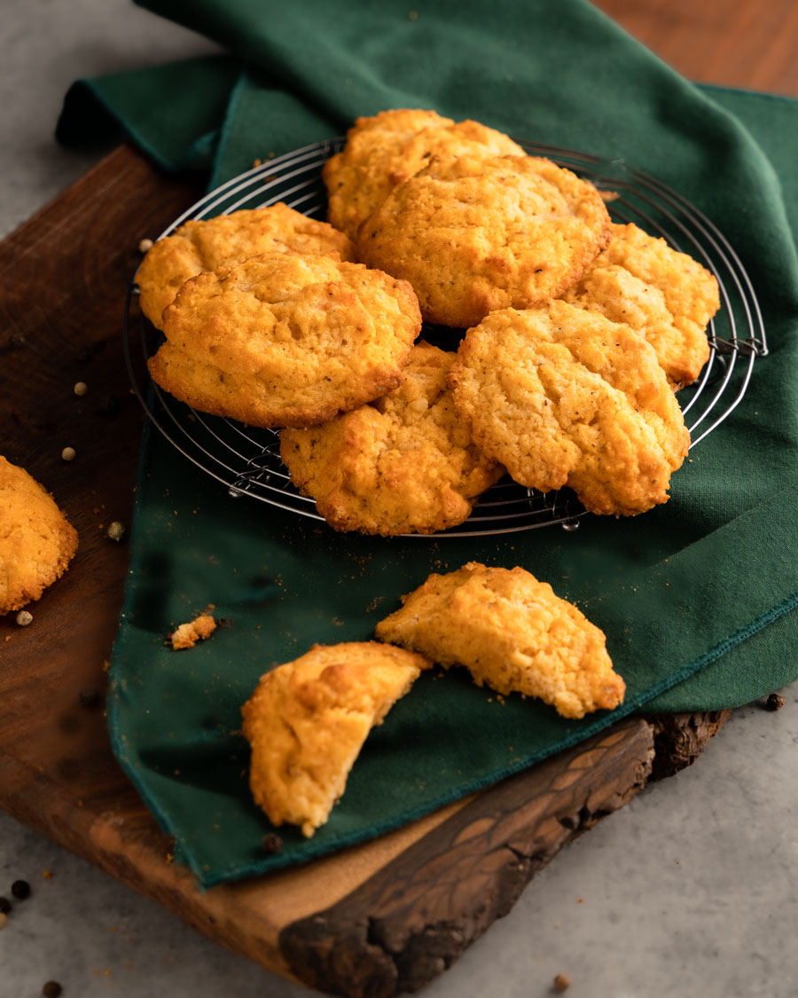Several biscuits sitting on a cooling rack with a cut biscuit in front.