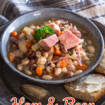3/4 view of a bowl of soup filled with ham, beans, and carrots.
