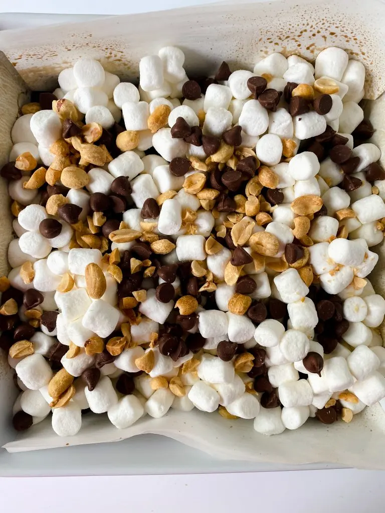 Miniature marshmallows, peanuts and chocolate chips on top of baked brownies.