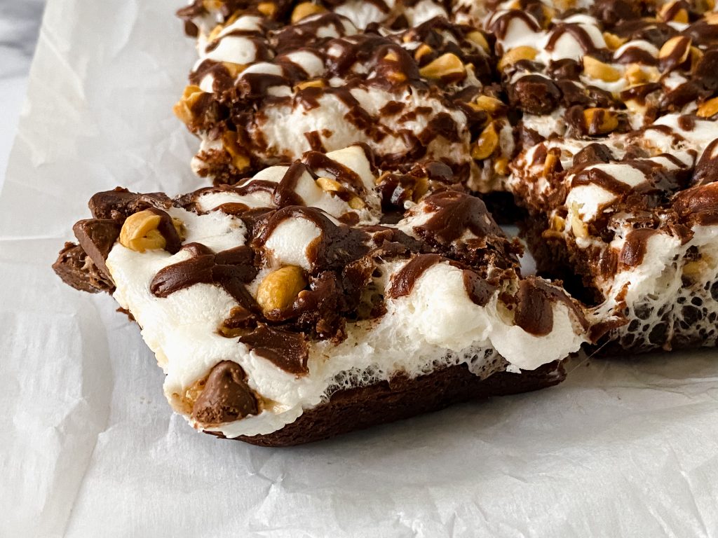 Side view of a brownie bar topped with melted marshmallows, peanuts and drizzled chocolate.