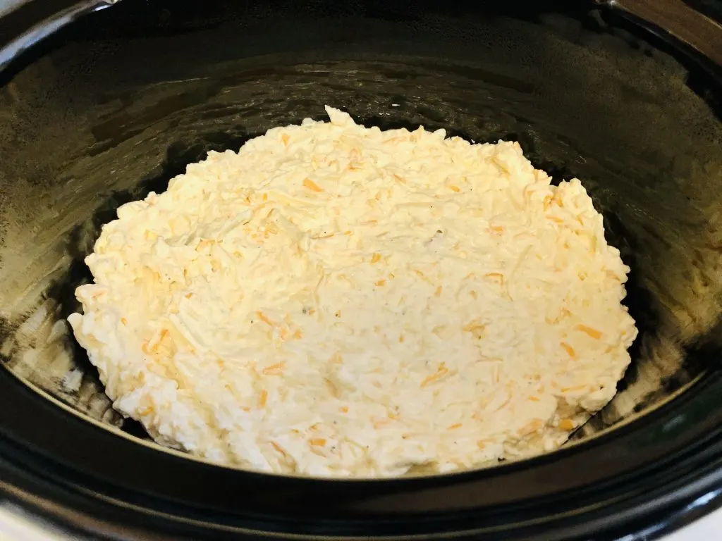 Hash brown casserole ingredients patted down in a slow cooker