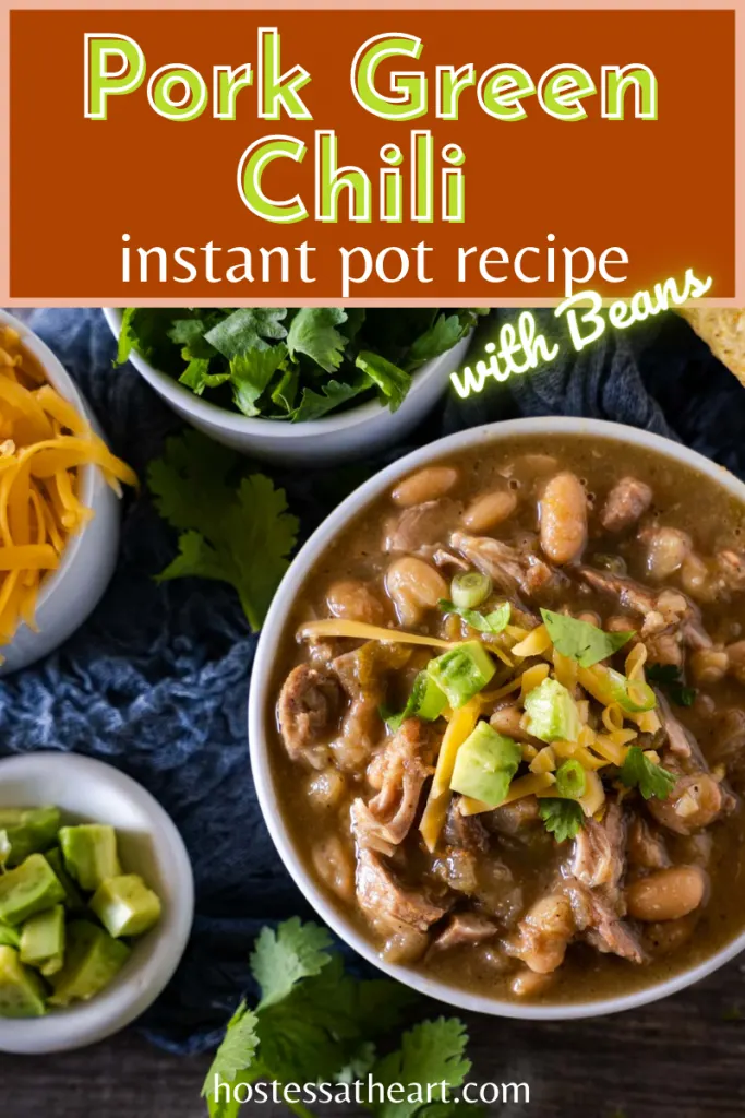 Top down view of a bowl of pork chili topped with avocado and cilantro with bowls of shredded cheese, cilantro, green onions, and tortilla chips off to the side.