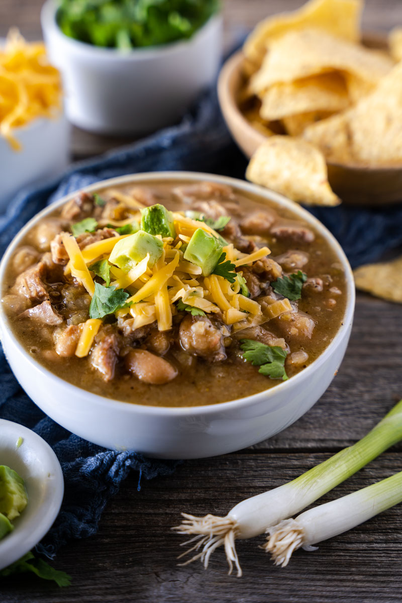 3/4 view of a bowl filled with green chili pork stew garnished with avocado, cilantro and cheese.