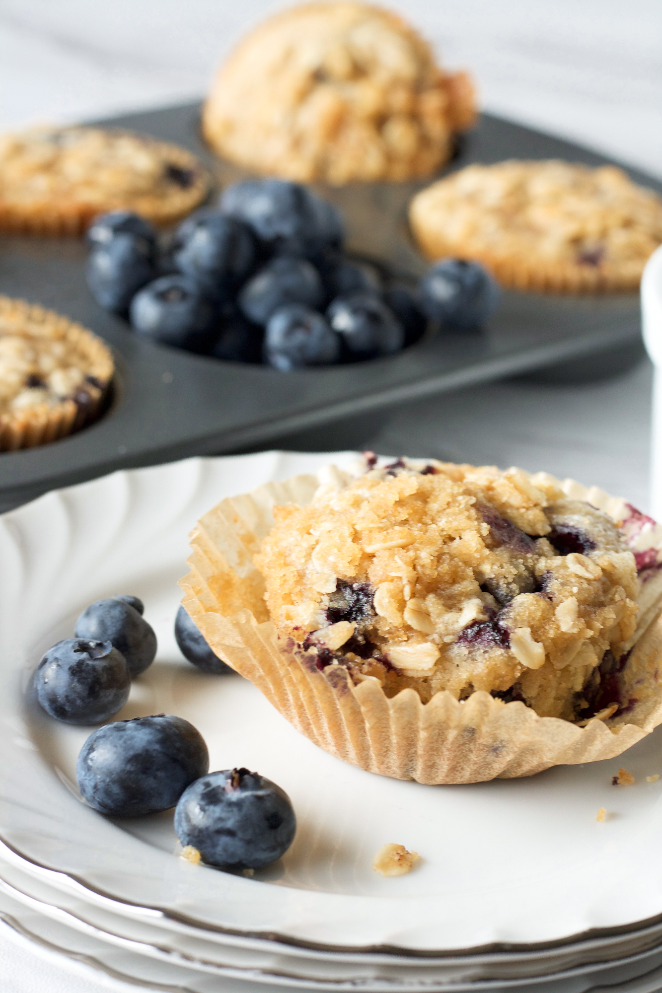 Side view of a sourdough discard blueberry muffin topped with streusel on a white plate. Hostess At Heart