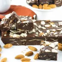 Close up view of a block of chocolate almond fudge with sliced pieces sitting on top and front.