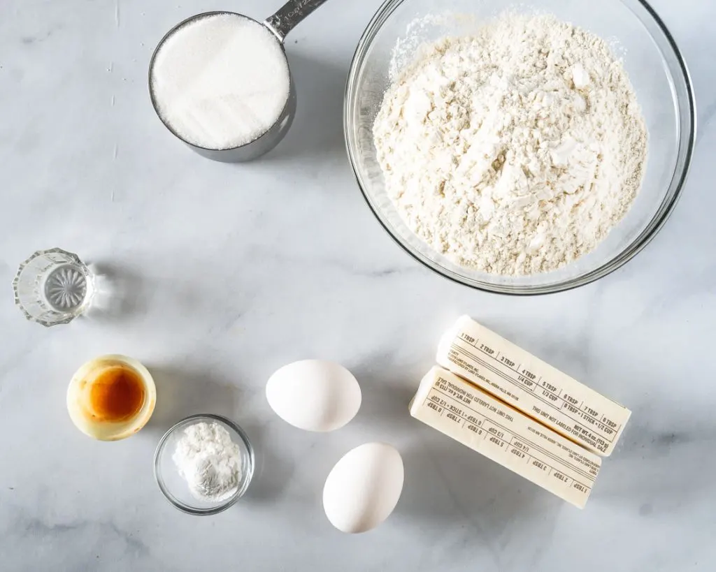 Ingredients to make crumbl cookies including flour, sugar, butter, eggs, baking powder, vanilla and almond extract.