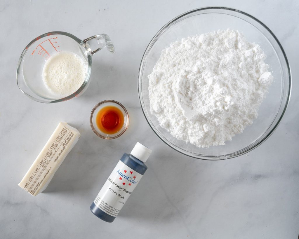 Ingredients used to make almond buttercream frosting including powdered sugar, cream, butter, and food coloring