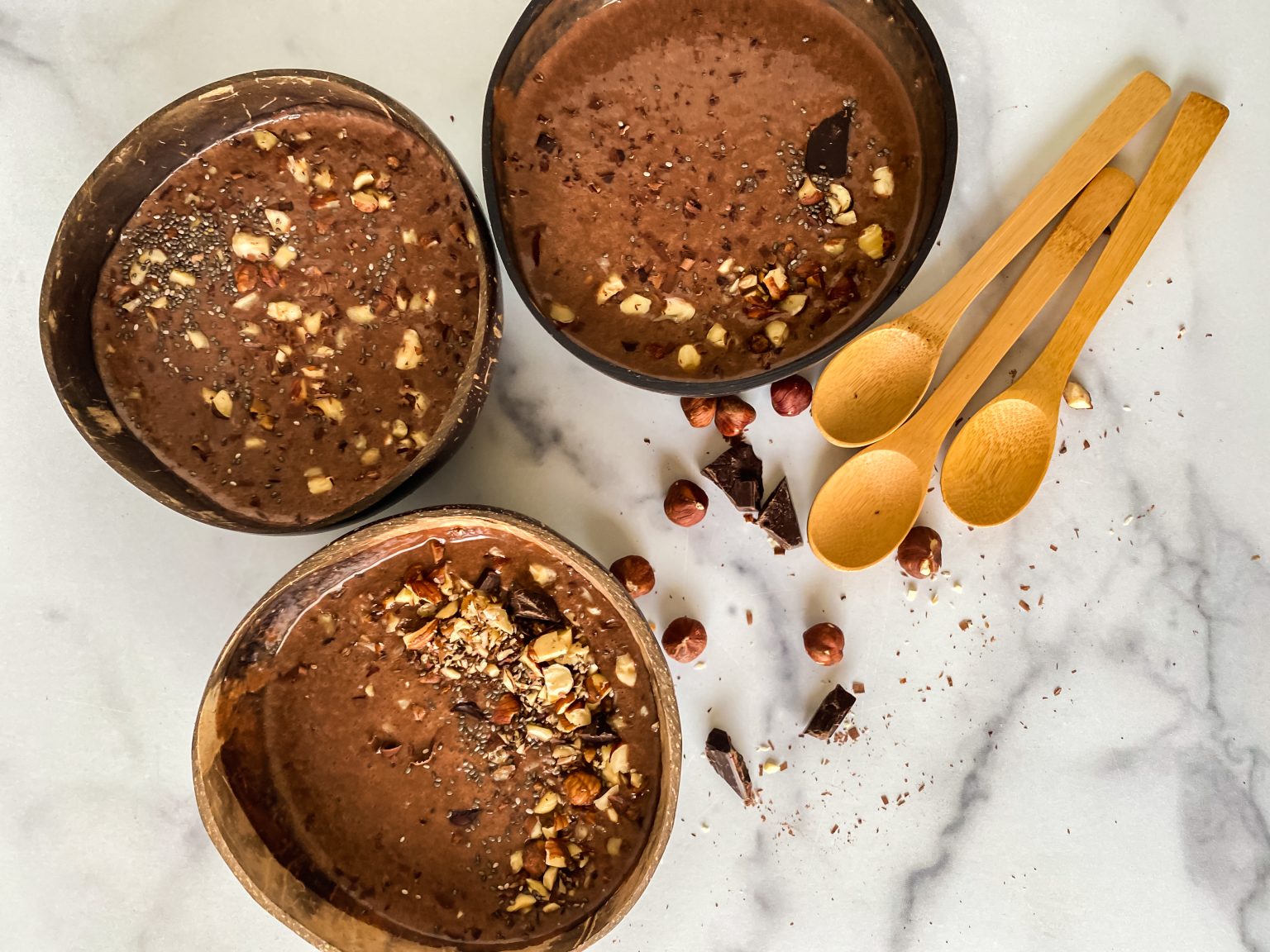 Top down view of three Chocolate Hazelnut Smoothie Bowls garnished with chopped hazelnuts and chocolate chunks.