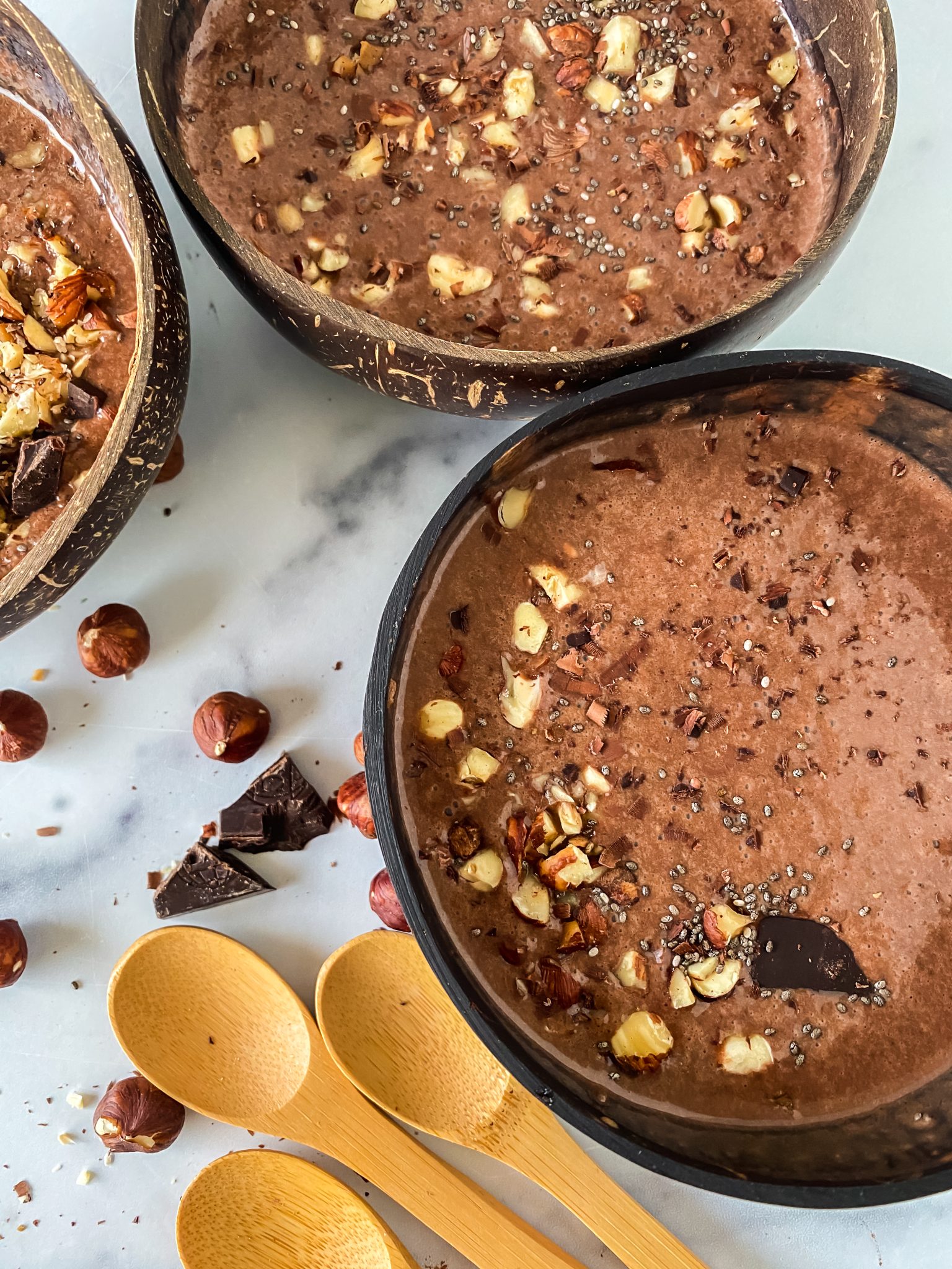 Top down view of three bowls of Chocolate Hazelnut Smoothies garnished with chopped hazelnuts.