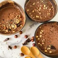 Close-up top down view of three bowls of chocolate smoothies topped with crushed hazelnuts.