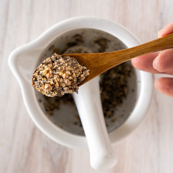 Crusted peppercorns, salt, and garlic making a paste sits on a wooden spoon.