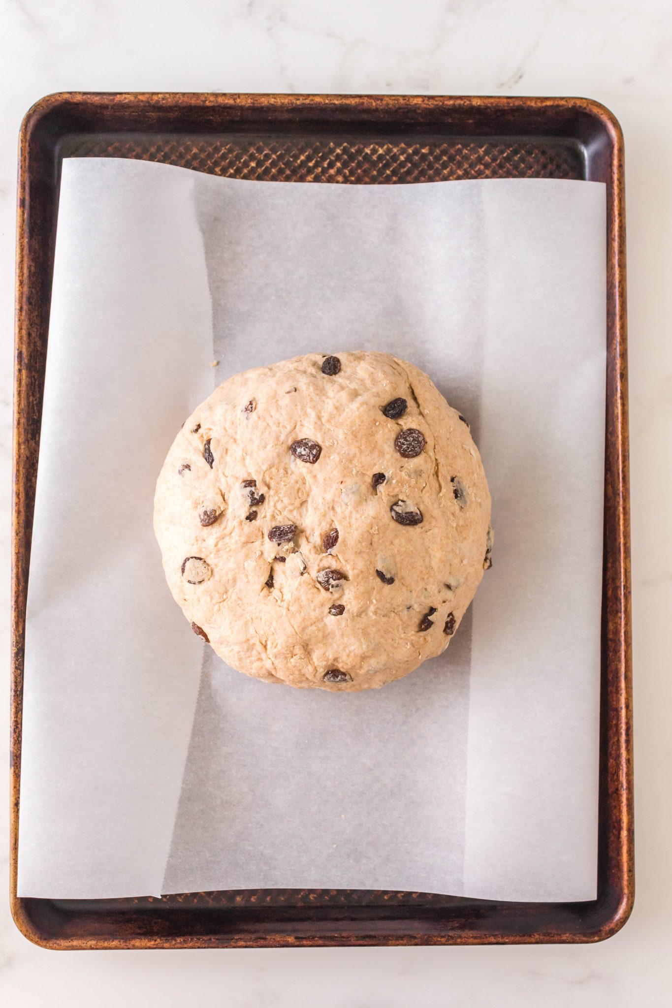 Top down view of a round shaped loaf of soda bread on a baking sheet.