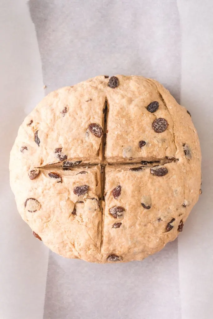 Top down view of a shaped loaf of soda bread with a cross cut into the top.