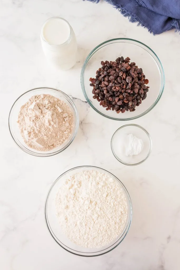 Ingredients used to make Irish Soda Bread including flour, baking soda, buttermilk, raisins and salt.