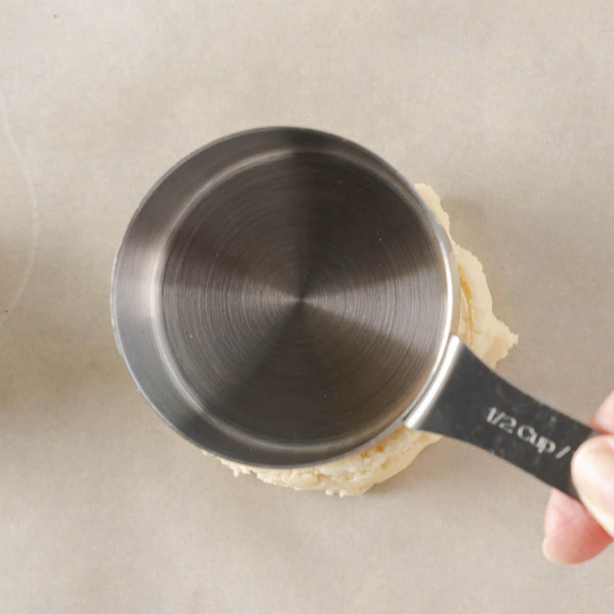 A measuring cup flattening a homemade crumbl sugar cookie before baking.