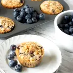 3/4 angle of a Blueberry Muffin topped with streusel sitting on a white plate.