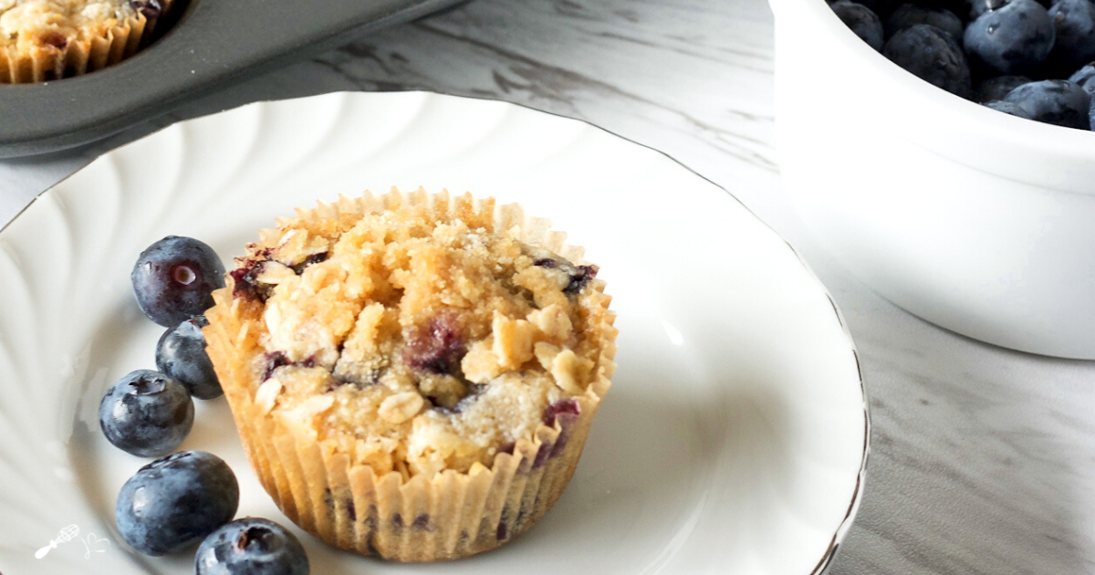 3/4 angle of a Blueberry Muffin topped with streusel sitting on a white plate.