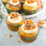 3/4 view of carrot cake cupcakes frosted and topped with crushed pecans and grated carrot.