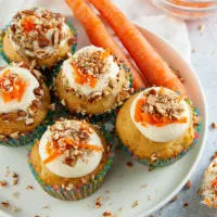 Top down photo of frosted cupcakes topped with grated carrot and chopped pecans on a plate.