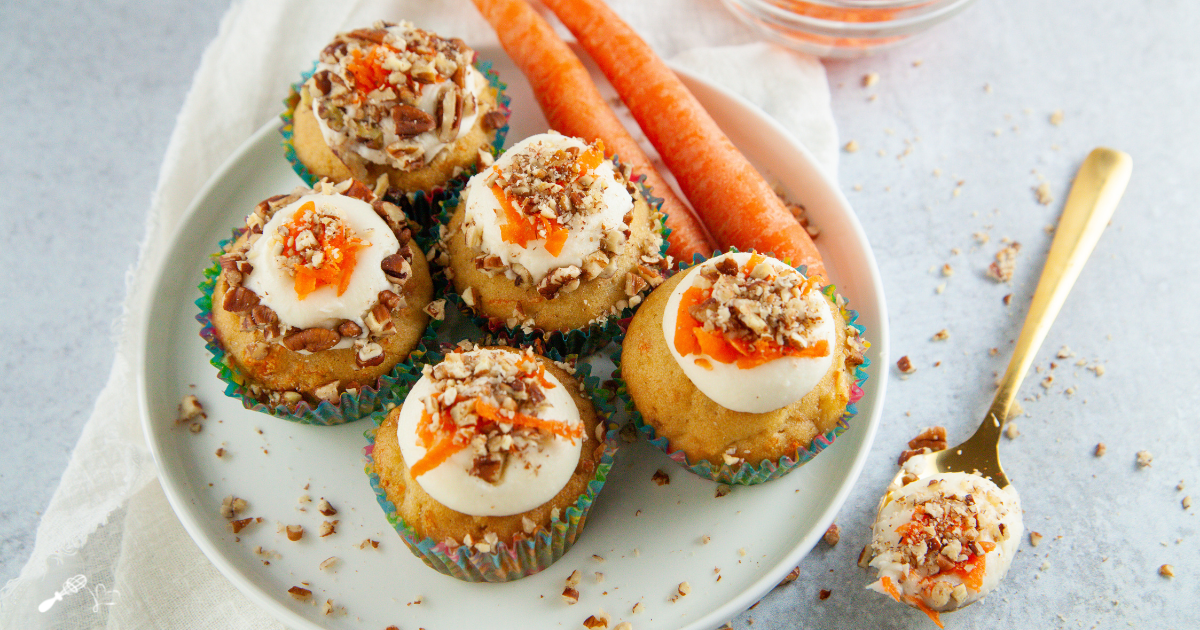 Top down photo of frosted cupcakes topped with grated carrot and chopped pecans on a plate.