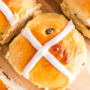 Side angle of a bread roll with a white glaze piped over the top in the shape of a cross.