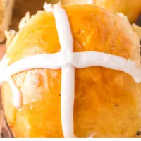 Top down view of a baked Hot Cross Bun with a white cross piped over the top.