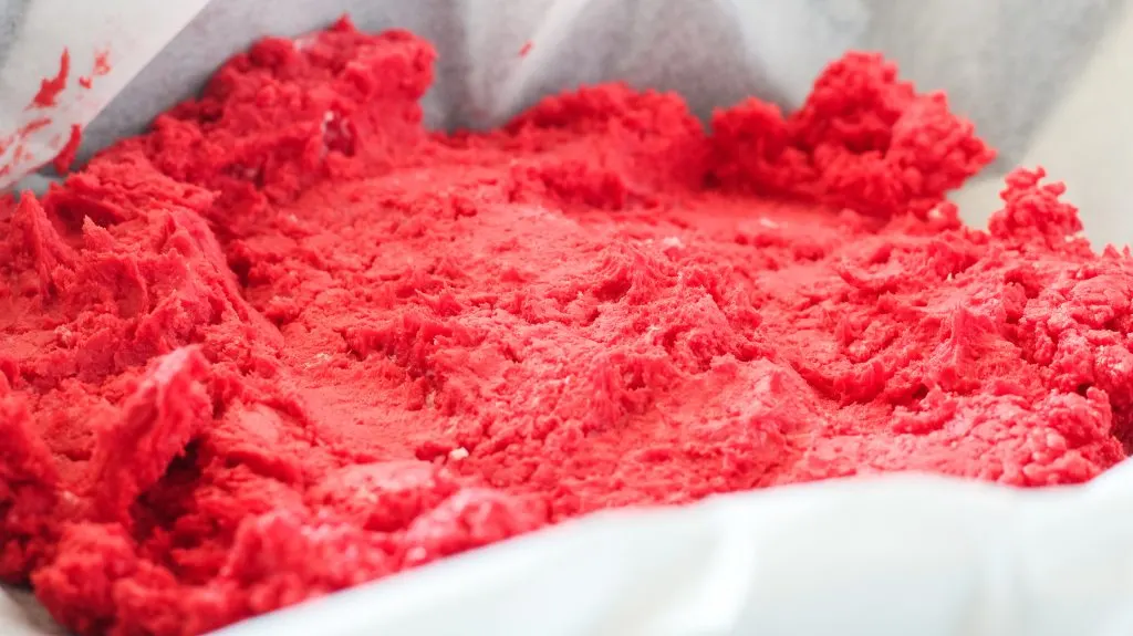 Red layer of fudge spread on the bottom of a parchment paper-lined pan.