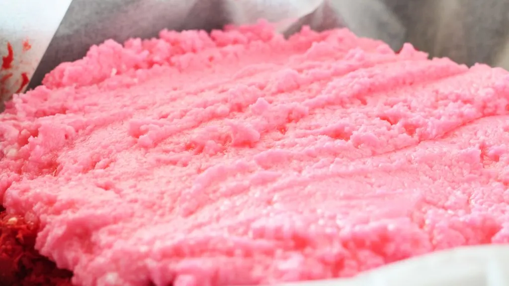 Pink colored fudge spread over a red layer of fudge.