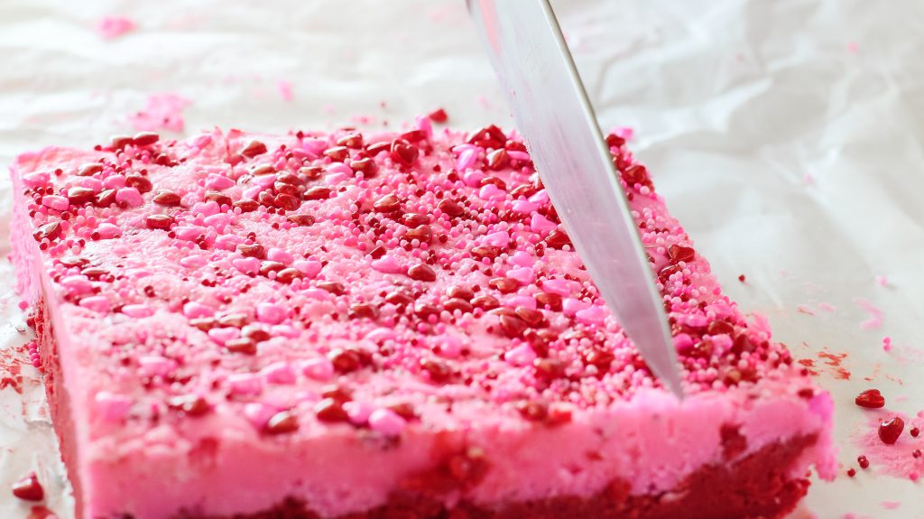 A sharp knife cutting into a two layered red and pink fudge - Hostess At Heart