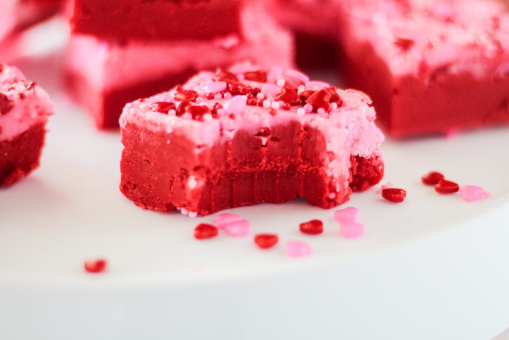 A piece of pink and red fudge sprinkled with hearts with a bite taken out of it.