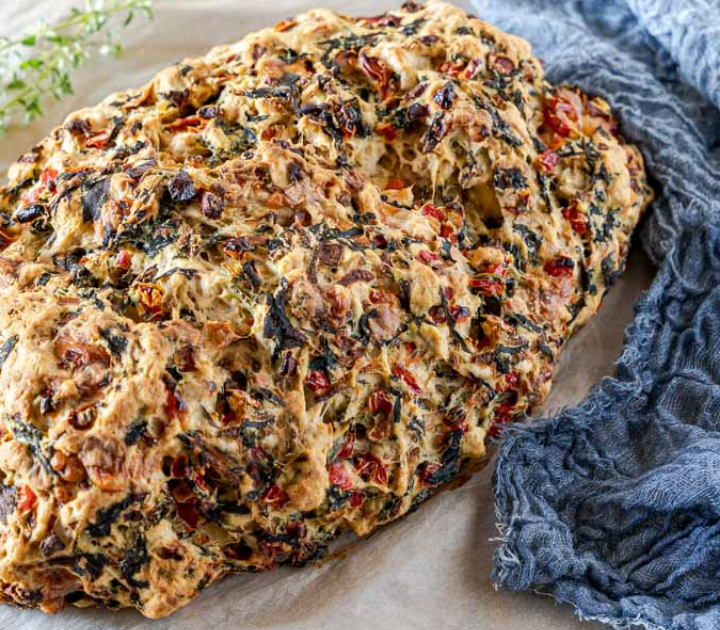 3/4 view of a loaf of bread loaded with cooked spinach, red pepper, and onion.
