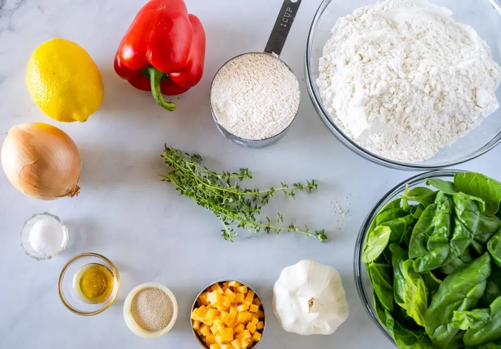 Ingredients are pictured: onion, flour, wheat flour, spinach, garlic, salt, olive oil, yeast, honey, red peppers, thyme, lemon juice, cheddar, butter.