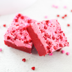 Two pieces of red and pink fudge stacked against each other with sprinkles on top.