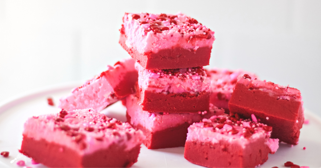 Pieces of red and pink fudge sprinkled with hearts that are stacked on top of each other.