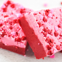 Two pieces of red and pink fudge sprinkled with hearts that are stacked next to each other.