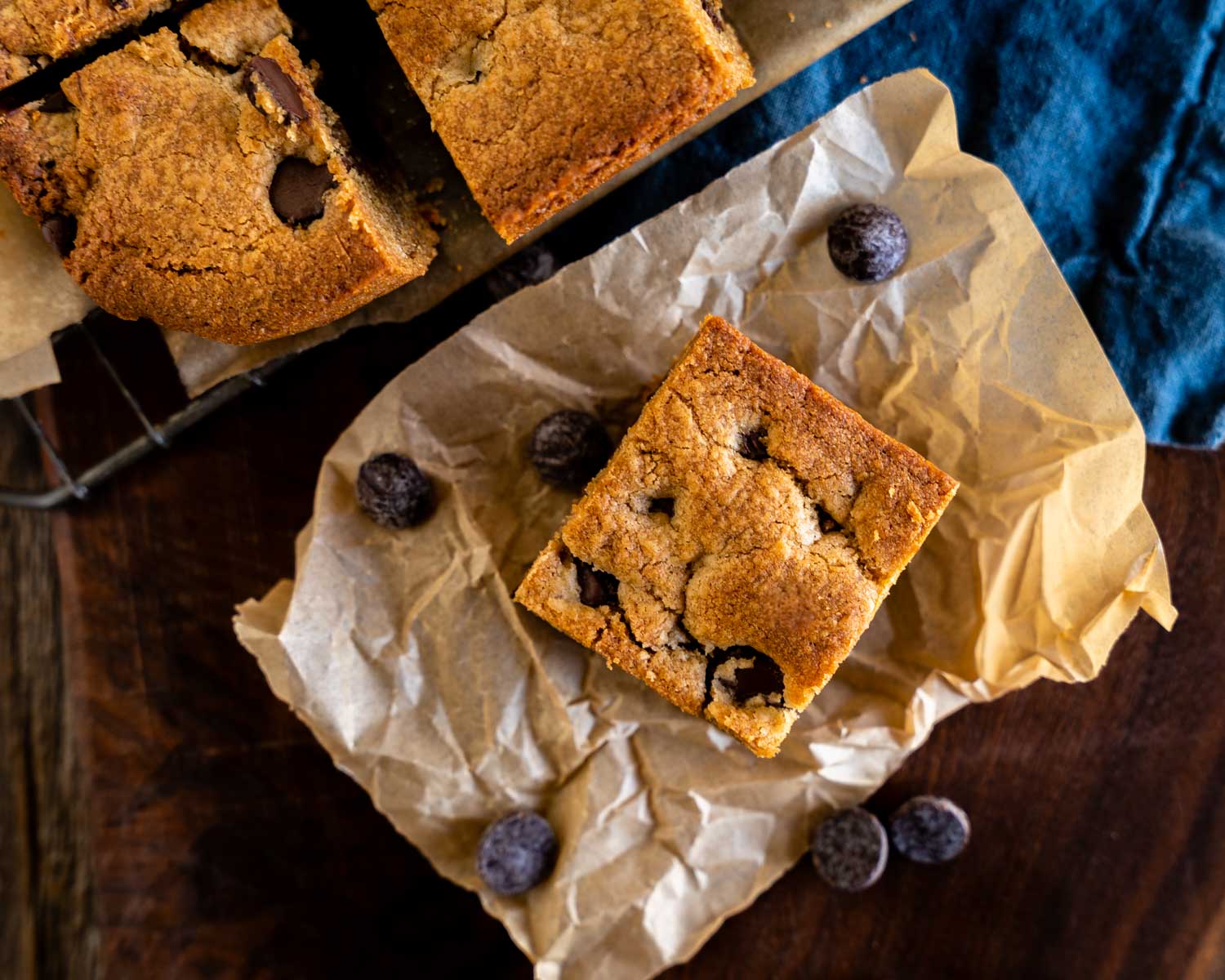 Top down view of a Peanut Butter Blondie bar filled with chocolate chips sitting on a piece of parchment paper and surrounded with chocolate chips.